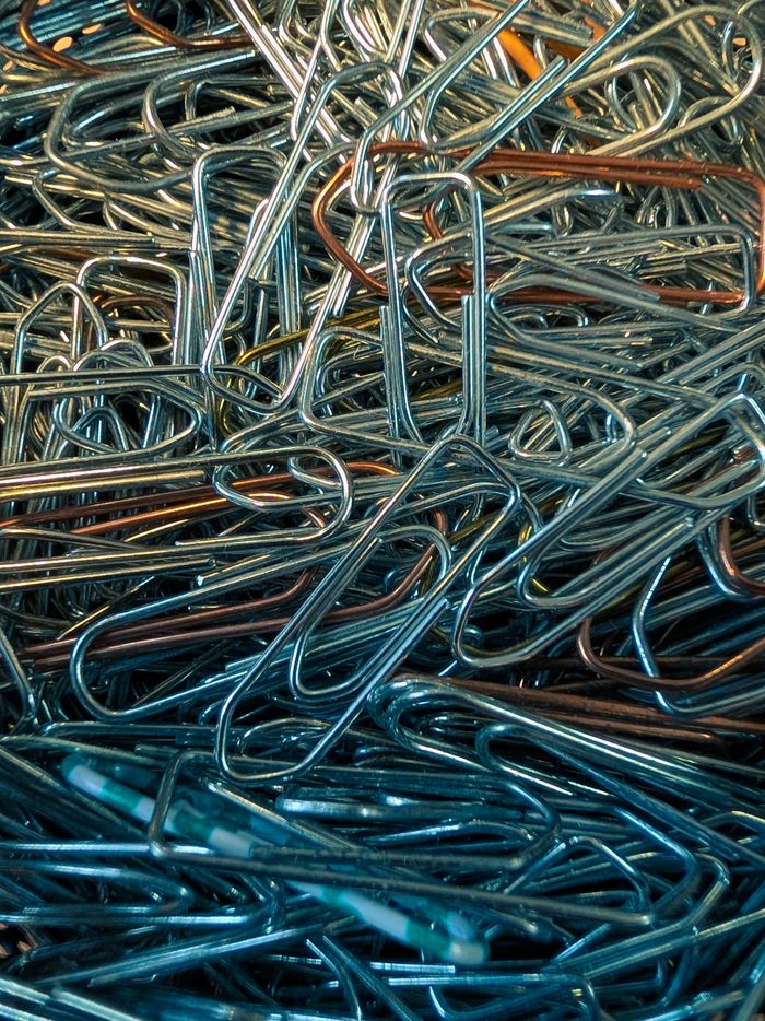 A pile of colorful metal paperclips in a closeup view, showcasing their textures and hues.