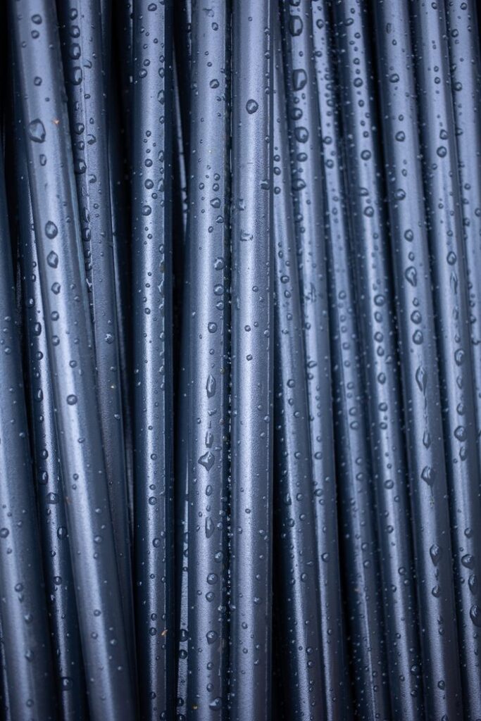 An abstract close-up of vertically arranged wet black pipes with raindrops.