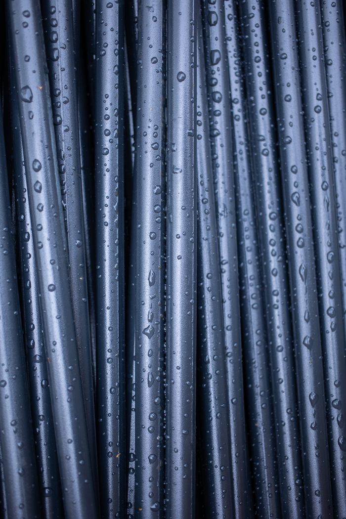 An abstract close-up of vertically arranged wet black pipes with raindrops.